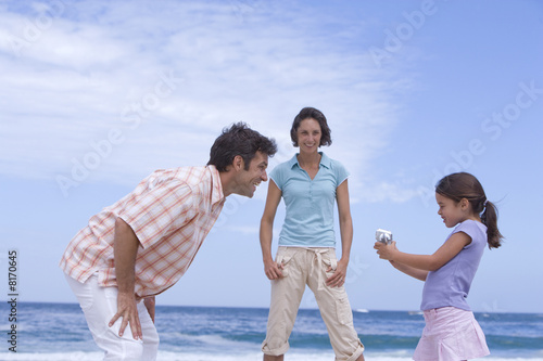 Photo: Parents smiling at daughter (6-8) with camcorder on beach, low angle view Parents smiling at daughter (6-8) with camcorder on beach, low angle view
