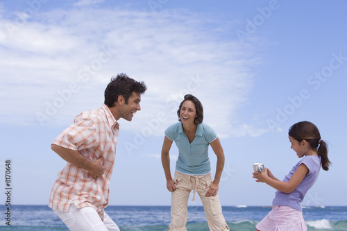 Photo: Family of three on beach, daughter (6-8) with camcorder, low angle view Family of three on beach, daughter (6-8) with camcorder, low angle view