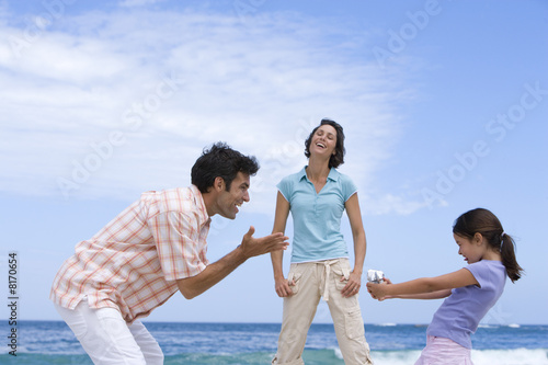 Photo: Family of three on beach, daughter (6-8) with camcorder, low angle view Family of three on beach, daughter (6-8) with camcorder, low angle view