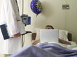 Doctor by man using laptop computer in hospital bed