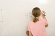 Girl (9-11) writing formula on whiteboard, rear view
