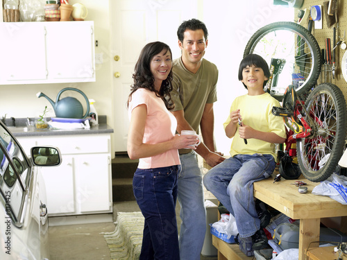 Photo: Family of three fixing bicycle in garage, smiling, portrait Family of three fixing bicycle in garage, smiling, portrait