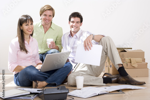 Photo: Woman with laptop by colleagues on floor by boxes, portrait Woman with laptop by colleagues on floor by boxes, portrait