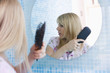 Young woman brushing hair in mirror