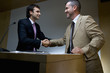 Businessman shaking hands with colleague by lectern, low angle view
