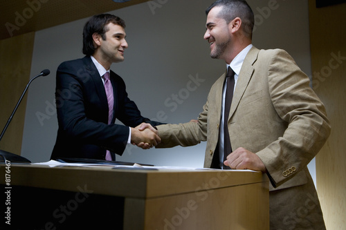 Photo: Businessman shaking hands with colleague by lectern, low angle view Businessman shaking hands with colleague by lectern, low angle view