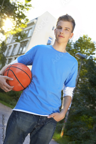 Foto: A teenage boy standing with a basketball. A teenage boy standing with a basketball.