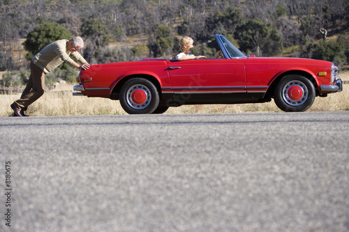 Photo: Man pushing broken down red convertible while wife steers Man pushing broken down red convertible while wife steers