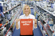 Young woman in electronics aisle holding 'special offer' sign, smiling, porttrait