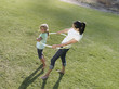 Photo: Mother and daughter (6-8) playing with hula hoop on grass in park, smiling, side view, elevated view Mother and daughter (6-8) playing with hula hoop on grass in park, smiling, side view, elevated view