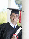 Photo: University student in graduation gown and mortar board holding diploma, smiling, close-up, portrait University student in graduation gown and mortar board holding diploma, smiling, close-up, portrait