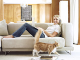 Photo: Woman with headphones and laptop relaxing on sofa at home, smiling, portrait, cat walking on carpet Woman with headphones and laptop relaxing on sofa at home, smiling, portrait, cat walking on carpet