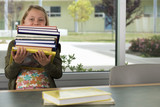 Photo: Girl (9-11) carrying stack of books in classroom, face obscured, front view, portrait Girl (9-11) carrying stack of books in classroom, face obscured, front view, portrait