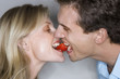 Affectionate couple sharing single strawberry, mouth to mouth, close-up, profile