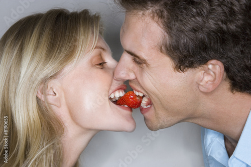 Foto: Affectionate couple sharing single strawberry, mouth to mouth, close-up, profile Affectionate couple sharing single strawberry, mouth to mouth, close-up, profile