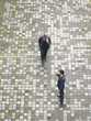 Two businessmen walking across a place and talking on the cellphone.