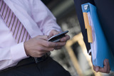 Photo: Businessman using personal electronic organiser, second man carrying file, close-up, mid-section Businessman using personal electronic organiser, second man carrying file, close-up, mid-section