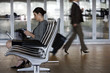 Photo: Businesswoman sitting in waiting area, using laptop and electronic organiser, profile Businesswoman sitting in waiting area, using laptop and electronic organiser, profile