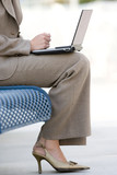 Photo: Businesswoman in suit and high heels using laptop on pavement bench, low section, profile Businesswoman in suit and high heels using laptop on pavement bench, low section, profile