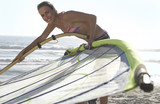 Photo: Young woman in bikini assembling windsurfer on sandy beach, smiling, side view, portrait Young woman in bikini assembling windsurfer on sandy beach, smiling, side view, portrait