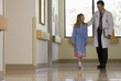 Photo: Doctor walking with patient in hospital corridor, girl (10-12) wearing dressing gown, smiling Doctor walking with patient in hospital corridor, girl (10-12) wearing dressing gown, smiling