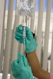 Photo: Nurse in green surgical gloves checking IV drip in hospital room, side view, close-up Nurse in green surgical gloves checking IV drip in hospital room, side view, close-up