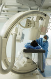 Photo: Doctor in blue surgical scrubs and mask operating medical scanner, patient lying on examination table Doctor in blue surgical scrubs and mask operating medical scanner, patient lying on examination table