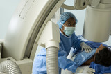 Photo: Doctor in blue surgical scrubs and mask operating medical scanner, patient lying on examination table Doctor in blue surgical scrubs and mask operating medical scanner, patient lying on examination table