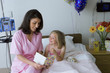 Photo: Nurse in pink scrubs sitting beside girl (6-8) in hospital bed, reading 'get well' card, smiling Nurse in pink scrubs sitting beside girl (6-8) in hospital bed, reading 'get well' card, smiling