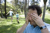 Photo: Family playing hide and seek in park, boy (9-11) and mother running, man covering eyes in foreground Family playing hide and seek in park, boy (9-11) and mother running, man covering eyes in foreground