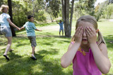 Photo: Family playing hide and seek in park, focus on girl (8-10) covering eyes in foreground Family playing hide and seek in park, focus on girl (8-10) covering eyes in foreground