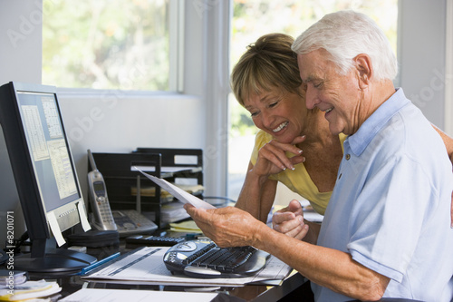 Couple in home office with computer and paperwork smiling