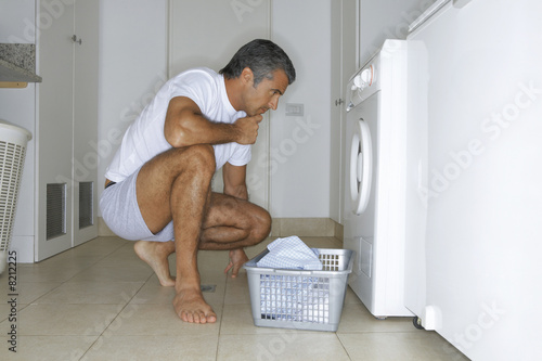 Photo: Man putting clothes in the washing machine. Man putting clothes in the washing machine.