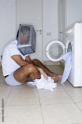 Photo: Man sitting in front of washing machine with a basket on his head Man sitting in front of washing machine with a basket on his head