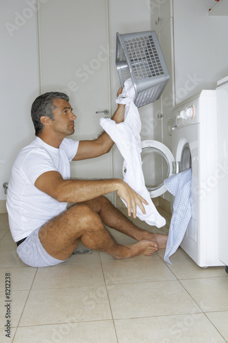 Photo: Man putting clothes in the washing machine. Man putting clothes in the washing machine.