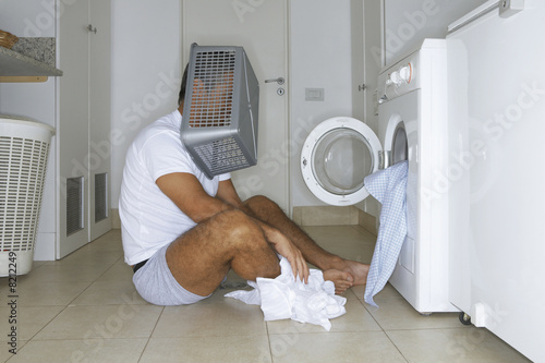Photo: Man sitting in front of washing machine with a basket on his head Man sitting in front of washing machine with a basket on his head