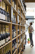 Photo: Female customer shopping in off-licence, looking at bottles of wine on shelf, tip-toeing, profile Female customer shopping in off-licence, looking at bottles of wine on shelf, tip-toeing, profile