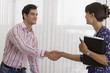 Photo: Businesswoman and businessman shaking hands in office, woman holding folder, smiling, side view Businesswoman and businessman shaking hands in office, woman holding folder, smiling, side view