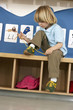 Photo: Blonde boy (4-6) sitting on bench in classroom, tying shoelace, alphabet cards on wall (tilt) Blonde boy (4-6) sitting on bench in classroom, tying shoelace, alphabet cards on wall (tilt)