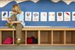 Photo: Blonde boy (4-6) sitting on bench in classroom, tying shoelace, alphabet cards on wall Blonde boy (4-6) sitting on bench in classroom, tying shoelace, alphabet cards on wall