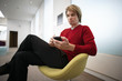 Photo: Businessman sitting on chair in office lobby, using personal electronic organiser, side view Businessman sitting on chair in office lobby, using personal electronic organiser, side view