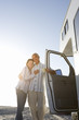 Photo: Mature couple arm in arm by motor home on beach, smiling, low angle view (sun flare) Mature couple arm in arm by motor home on beach, smiling, low angle view (sun flare)