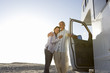 Photo: Mature couple arm in arm by motor home on beach, smiling, portrait, low angle view (sun flare) Mature couple arm in arm by motor home on beach, smiling, portrait, low angle view (sun flare)