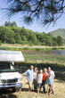 Photo: Family of three generations arm in arm by motor home by lake, smiling, portrait, elevated view Family of three generations arm in arm by motor home by lake, smiling, portrait, elevated view