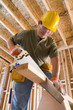Builder in hardhat sawing, low angle view