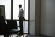 Photo: Businessman looking through window in conference room, waiting to begin presentation, rear view Businessman looking through window in conference room, waiting to begin presentation, rear view