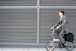 Photo: Businessman cycling on folding commuter bicycle on pavement, profile Businessman cycling on folding commuter bicycle on pavement, profile