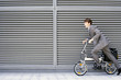 Photo: Businessman cycling on folding commuter bicycle on pavement, profile Businessman cycling on folding commuter bicycle on pavement, profile
