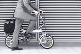 Photo: Businessman cycling on folding commuter bicycle on pavement, side view, low section Businessman cycling on folding commuter bicycle on pavement, side view, low section