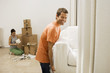 Photo: Couple moving house, man lifting white sofa through doorway, woman packing boxes in sparse room Couple moving house, man lifting white sofa through doorway, woman packing boxes in sparse room